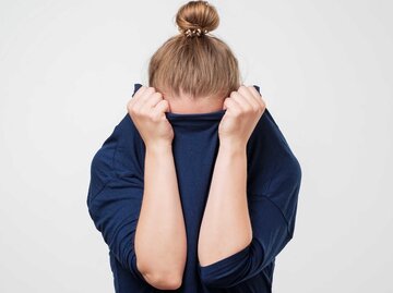 Frau verbirgt schüchtern ihren Kopf in ihrem Pulli | © Getty Images/Koldunova_Anna
