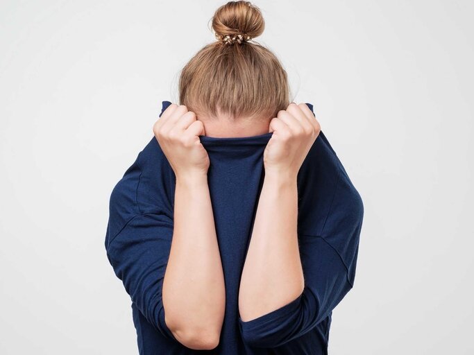 Frau verbirgt schüchtern ihren Kopf in ihrem Pulli | © Getty Images/Koldunova_Anna