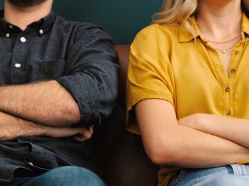 Mann und Frau sitzen mit verschränkten Armen nebeneinander auf dem Sofa | © Getty Images/shapecharge