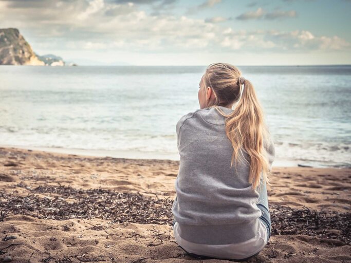 Frau sitzt am Strand | © Getty Images/splendens