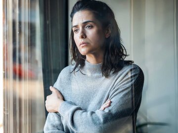 Frau steht nachdenklich vor einem Fenster und blickt hinaus | © Getty Images/Westend61