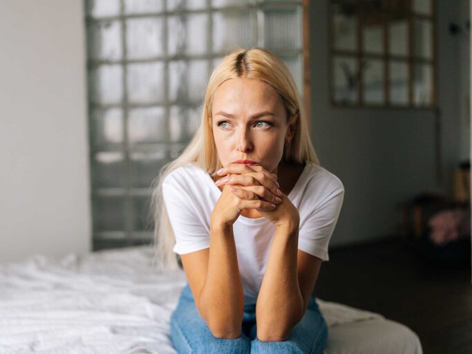 Porträt einer depressiven Frau, die allein zu Hause sitzt und mit traurigem Gesichtsausdruck wegschaut, Hände am Kinn haltend | © Getty Images/dikushin