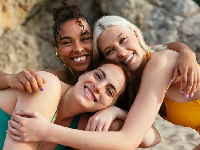 Drei glückliche Freundinnen, die sich am Strand aneinander lehnen | © Getty Images/Westend61