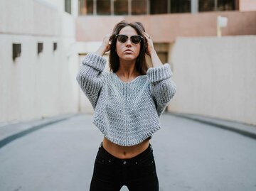 Frau steht mit breiten Beinen vor einem Haus und trägt cool eine Sonnenbrille. | © Unsplash / Brooke Cagle