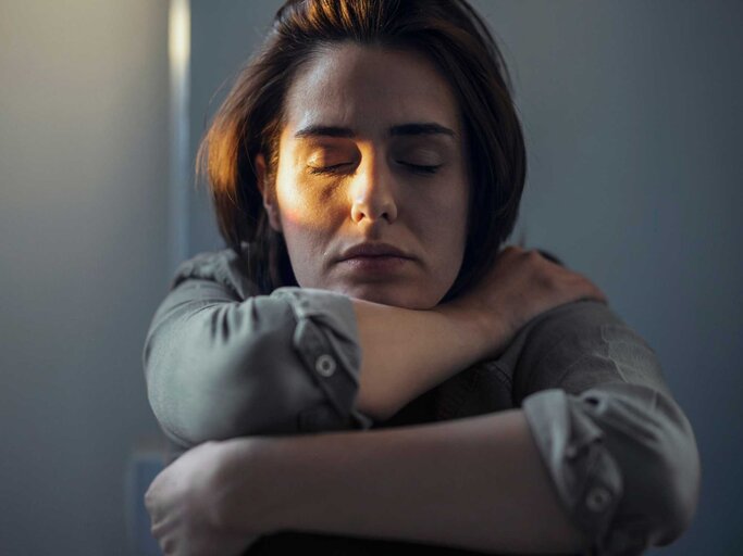 Frau sitzt mit geschlossenen Augen im Dunkeln | © Getty Images/Westend61
