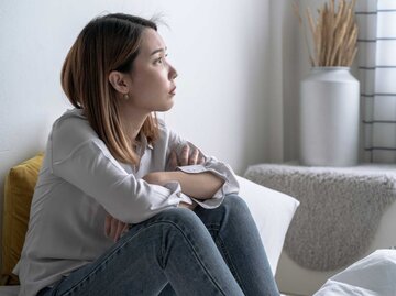 Junge Frau sitzt nachdenklich auf der Couch | © Getty Images/Panupong Piewkleng