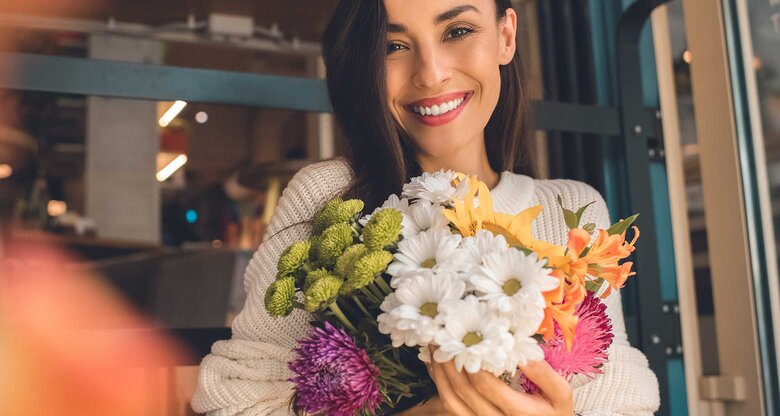 Frau mit hellem Strickpullover hält einen Strauß verschiedener Blumen in der Hand. | © Adobe Stock/LIGHTFIELD STUDIOS