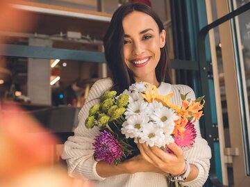 Frau mit hellem Strickpullover hält einen Strauß verschiedener Blumen in der Hand. | © Adobe Stock/LIGHTFIELD STUDIOS