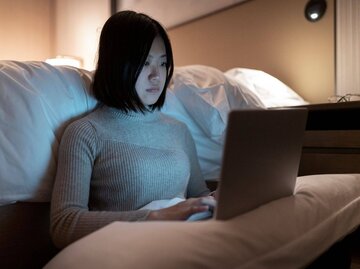 Person sitzt vor Bett an Laptop. | © Getty Images/Sammyvision
