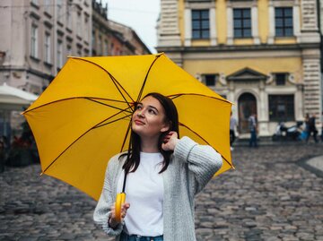 Glückliche Frau unter einem gelben Regenschirm | © Getty Images/Anna Blazhuk