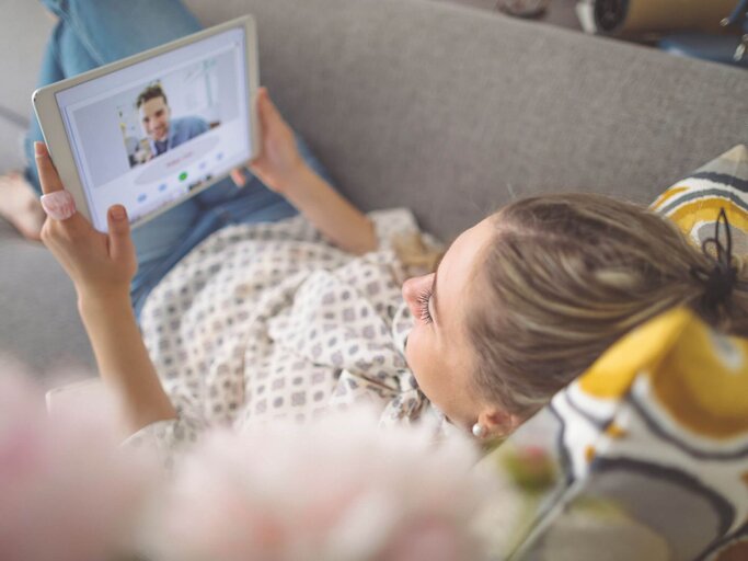 Person liegt auf Couch bei Videocall | © Getty Images/Eva-Katalin
