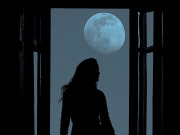 Frau steht bei Nacht am Fenster, es ist fast Vollmond. | © Adobe Stock/Maxim Chuev