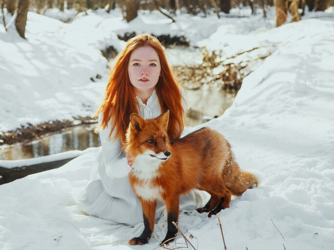 Eine junge rothaarige Frau mit einem Fuchs in der Natur | © Getty Images / Marie Dashkova 