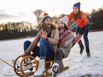 Gruppe von Freundinnen fährt zusammen Schlitten | © Getty Images/Westend61