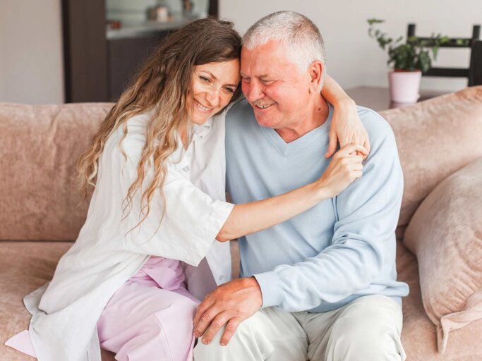 Erwachsene Tochter umarmt Vater auf der Couch. | © Adobe Stock/Tatyana Gladskih