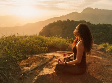 Junge Frau meditiert auf einem Berg bei Sonnenaufgang | © Getty Images/Ingo Roesler