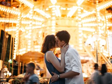 Frau und Mann küssen sich vor Karussell | © Getty Images/Igor Ustynskyy