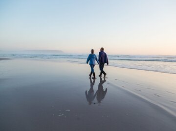 Älteres Paar geht Hand in Hand am Strand entlang | © Getty Images/Alistair Berg