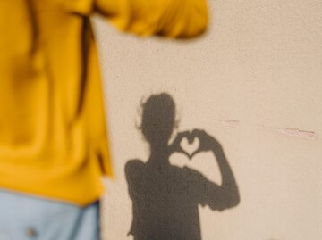 Frau steht ihrem Schatten gegenüber und formt Herz mit den Händen | © Getty Images/Westend61