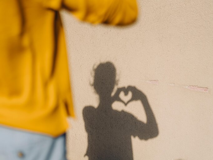Frau steht ihrem Schatten gegenüber und formt Herz mit den Händen | © Getty Images/Westend61
