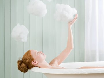 Frau sitzt in der Badewanne und berührt Schaumwolken | © Getty Images/Image Source