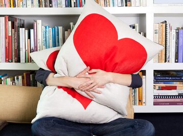 Frau hält zwei Kissen mit Herz-Druck fest an ihrem Körper | © Getty Images/Catherine Ledner