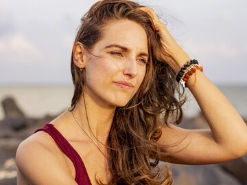 Junge Frau ist am Strand und schaut in die Ferne während der Wind durch ihre Haare weht | © Getty Images/CamBuff