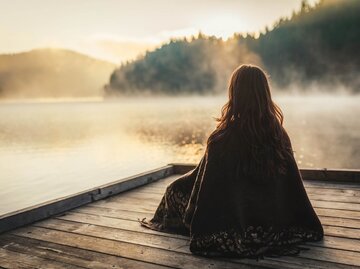 Frau sitzt auf Steg am See | © Getty Images/Vasil Dimitrov