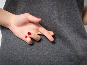 Hand mit roten Fingernägeln und gekreuzten Fingern hinterm Rücken | © Getty Images/Mikhail Azarov