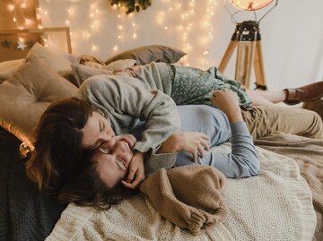 Liebespaar liegt auf dem Bett und Frau küsst Mann  | © Getty Images/Arina Krasnikova