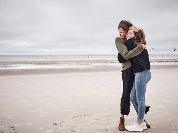 Frauen am Strand umarmen sich und lachen dabei | © Getty Images/Oliver Rossi