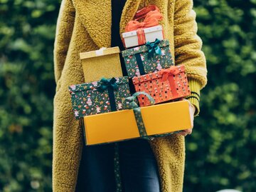 Frau in gelbem Mantel mit Weihnachtsgeschenken auf dem Arm | © Getty Images/Liliya Krueger