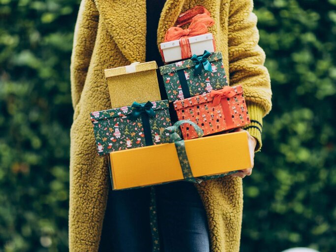 Frau in gelbem Mantel mit Weihnachtsgeschenken auf dem Arm | © Getty Images/Liliya Krueger