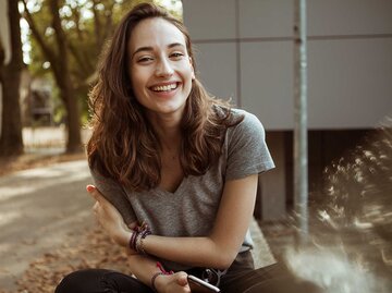 Eine junge Frau sitzt mit ihrem Handy in der Hand da und lacht glücklich. | © Getty Images / Westend61