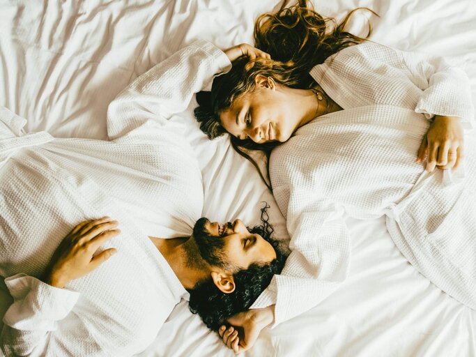 Frau und Mann in Bademantel auf Bett | © Getty Images/Maskot