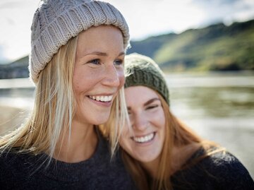 Portrait von zwei jungen Frauen mit Mützen an einem Fluss. | © Getty Images / Oliver Rossi