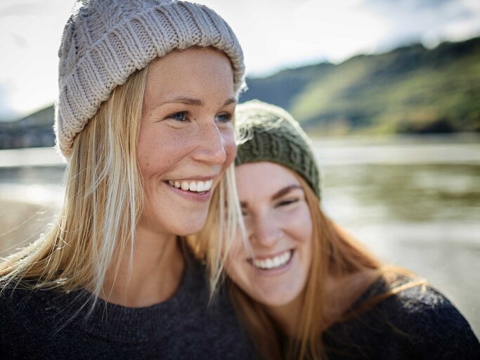Portrait von zwei jungen Frauen mit Mützen an einem Fluss. | © Getty Images / Oliver Rossi