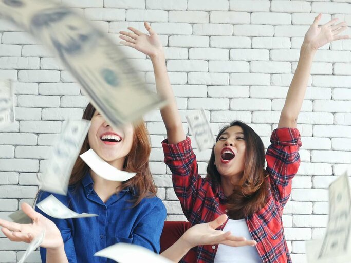 Glückliche Frauen werfen Geld in die Luft | © Getty Images/howtogoto