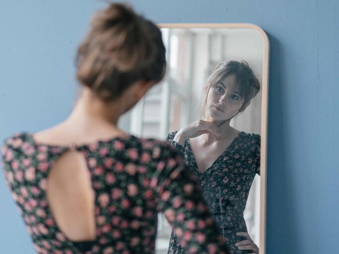 Junge Frau schaut verunsichert in den Spiegel | © Getty Images/Westend61