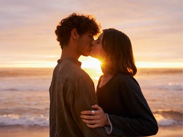 Junges Paar küsst sich am Strand vor dem Sonnenuntergang | © Getty Images/mapodile
