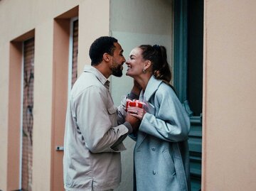 Man überreicht Partnerin ein Geschenk vor der Haustür | © Getty Images/Alina Rudya/Bell Collective