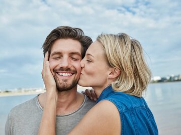 Frau mit blonden Haaren gibt einem Mann mit braunen Haaren einen leidenschaftlichen auf die Backe. | © Getty Images / Westend61