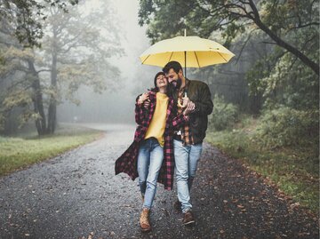 Pärchen unter einem gelben Regenschirm geht spazieren | © Getty Images/skynesher