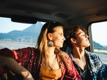 Junge Frau blickt aus dem Autofenster Richtung Sonnenuntergang. | © Getty Images/massimo colombo