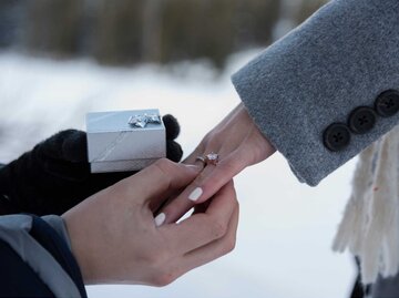 Mann steckt Ring an Frauenhand vor Schnee | © Adobe Stock
