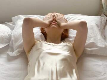 Junge Frau schlägt im Bett frustriert die Hände über die Augen | © Getty Images/Tara Moore