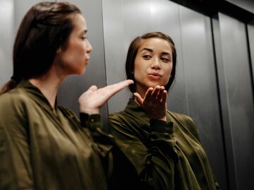 Junge Frau wirft ihrem Spiegelbild einen Kuss zu | © Getty Images/Westend61