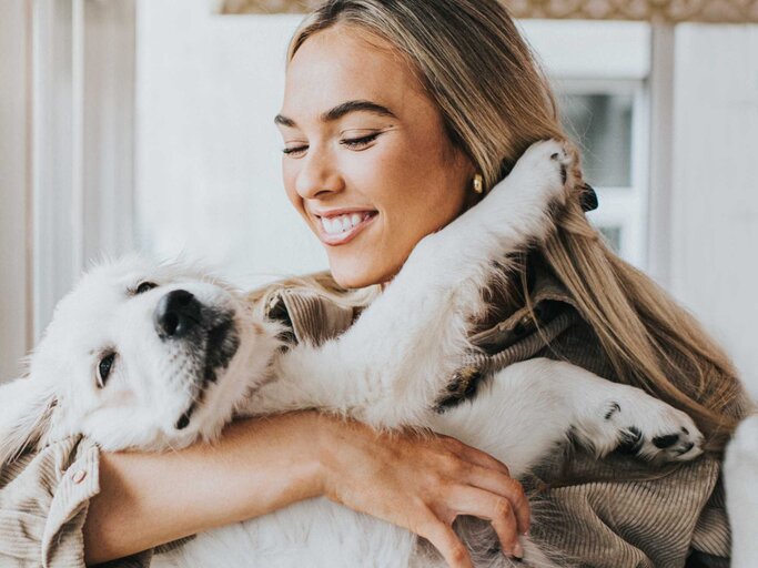 Frau trägt ihren Hund auf dem Arm und lächelt ihn an | © Getty Images/Catherine Falls Commercial