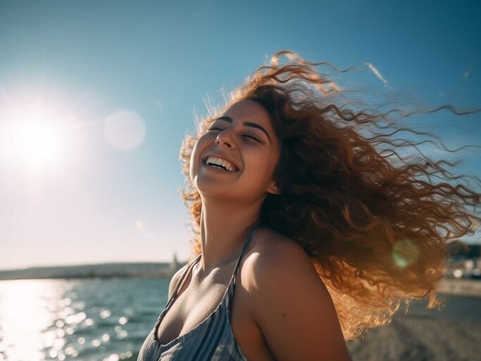 Glückliche Frau mit Locken am Strand | © Midjourney/Maxi Baumgärtner