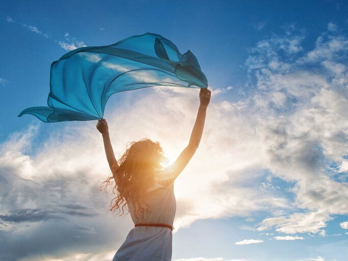 Frau hält Tuch in die Luft vor blauem Himmel | © Getty Images/Gilitukha